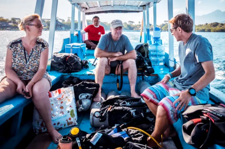 Three scuba divers on a traditional outrigger boat at Menjangan Island attending a dive briefing with their guide before diving