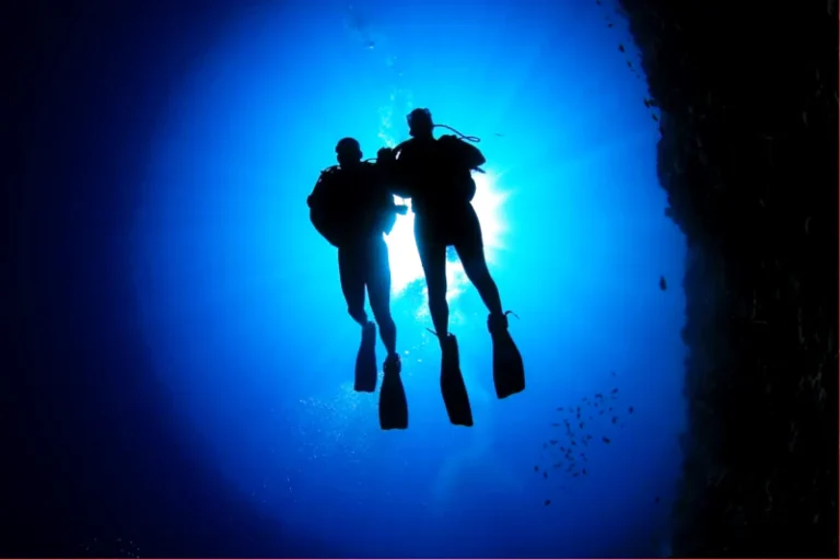 Two scuba divers underwater in Bali, seen from depth with blue water and natural light above them