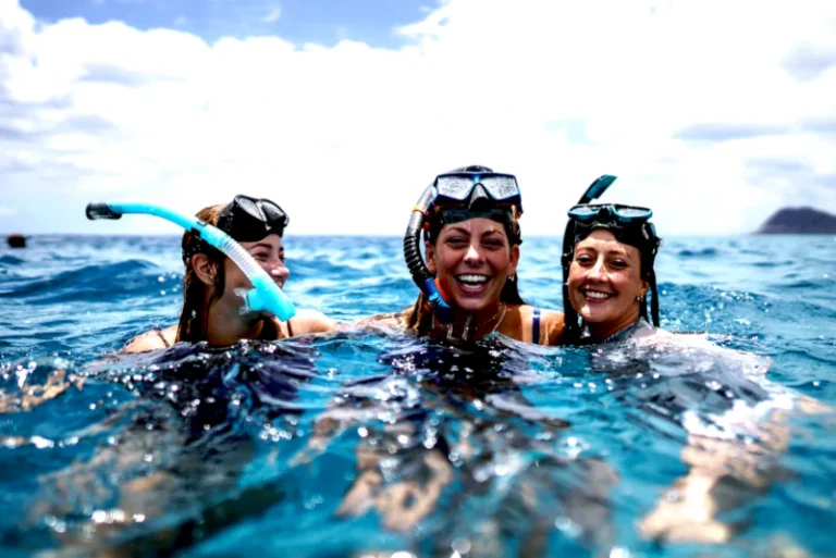 Three smiling women snorkeling in Bali at the surface with masks and snorkels during a guided snorkeling trip