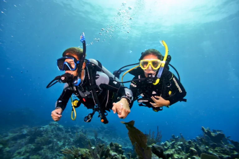 Two beginner divers holding hands underwater during a Discover Scuba Diving experience in Bali shallow water